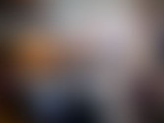 A group of people sit in a spacious room with exposed brick walls. A person stands speaking at the front. Colorful garlands decorate overhead.