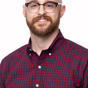 Smiling bald man with glasses and beard (Josh Murray) in a red plaid shirt against a white background