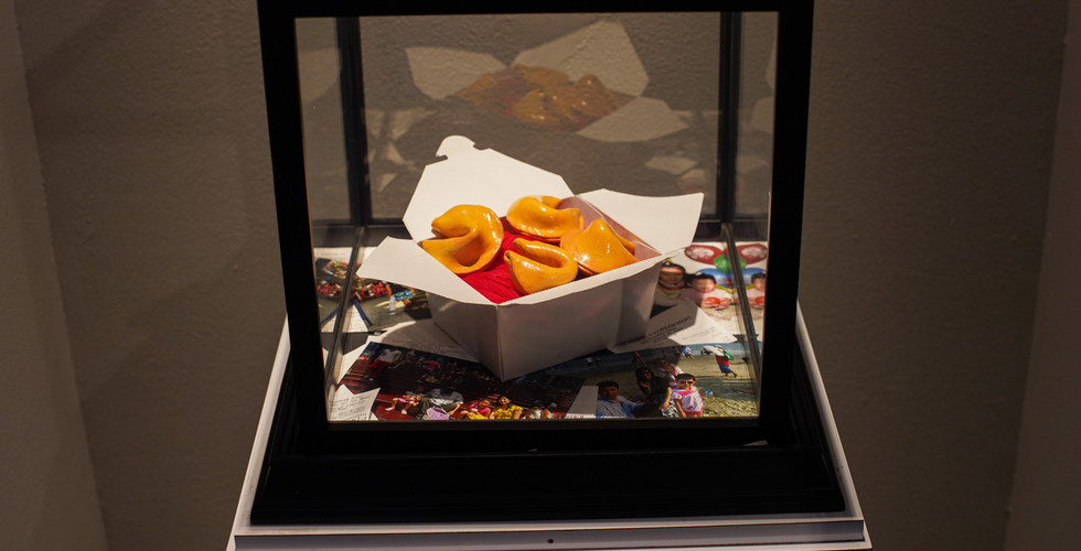 Fortune cookies in a takeout box are displayed in a glass case with family photos, creating a nostal