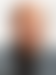 A professional headshot of a man with a shaved head and a groomed beard and mustache (John Jennings). He is wearing a grey plaid blazer over a black t-shirt, looking directly at the camera with a neutral expression against a white background.