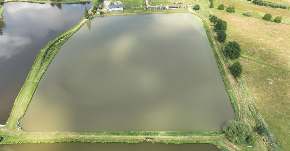 Aerial view of Nowiniec Staw Nr 3, a rectangular lake surrounded by grass.