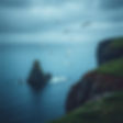 create a topical image with cliffs and seagulls in the distance. Make it using cool colors