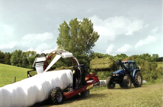 New Holland tractor loading large square hay bales into an Anderson inline bale wrapper