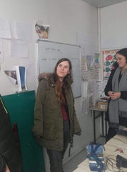 A woman is at the front of the classroom, listening to someone out of frame who is talking.