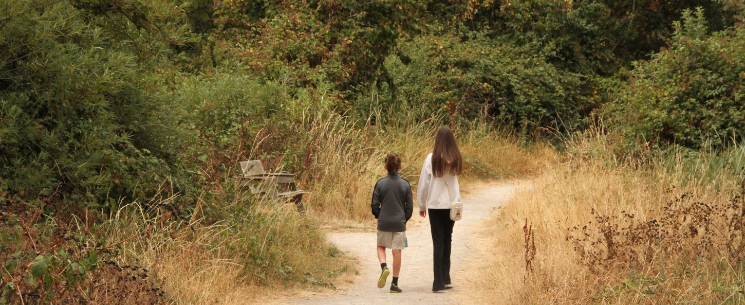 Young child and teenager walking along an accessible path at Coed y Morfa woodland in Prestatyn.