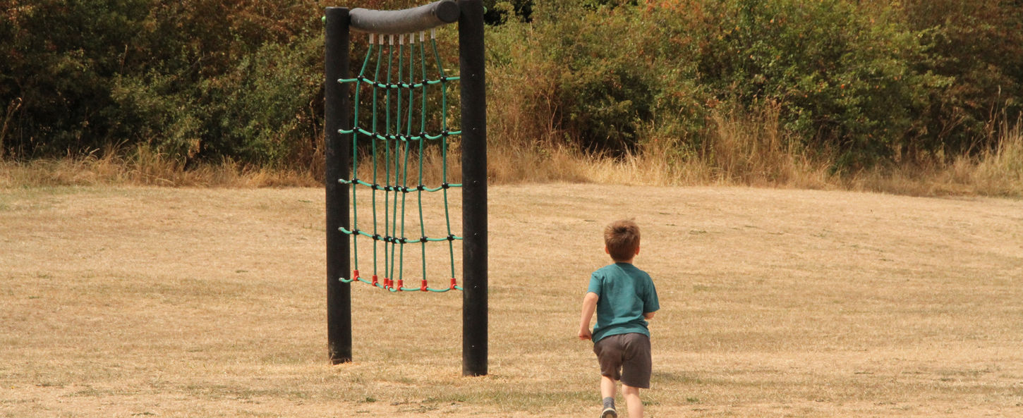 Child running towards outdoor play equipment in the open grassland area at Coed y Morfa.
