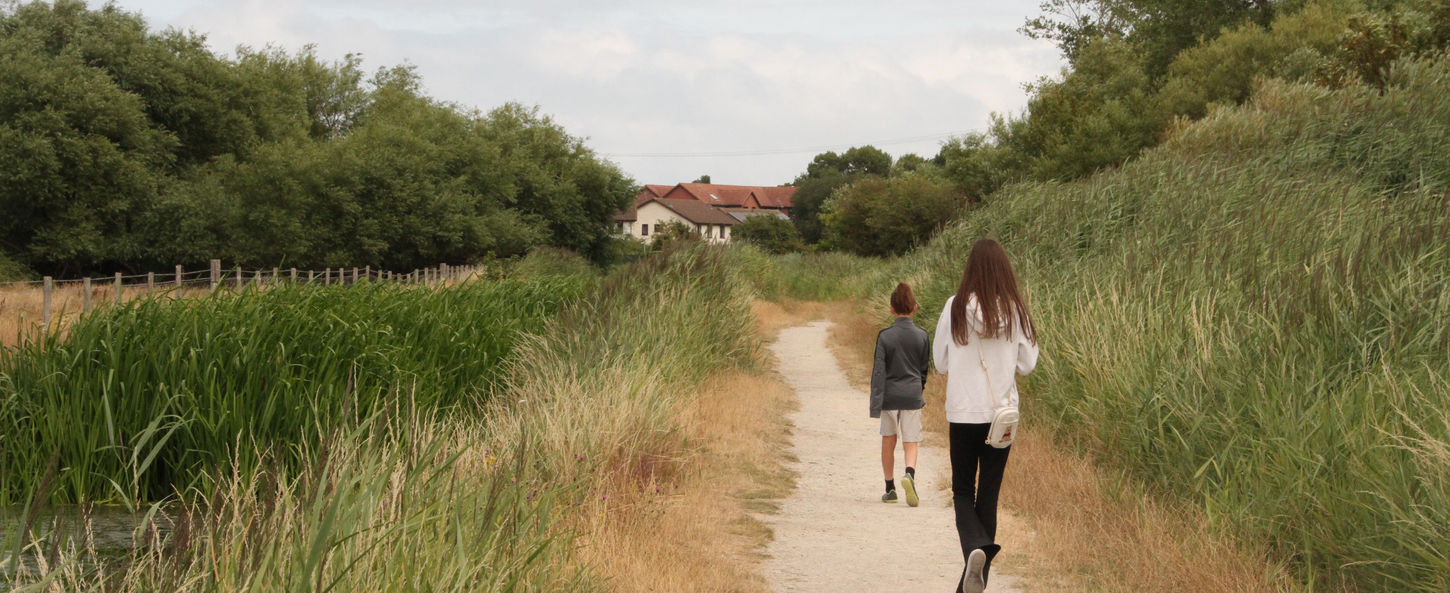 Child and teenager walking along a wide path through grassland at Coed y Morfa, Prestatyn.