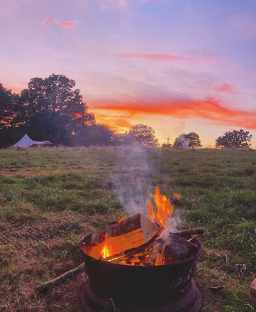 campfire on a grass pitch with a bell tent and sunset in the background