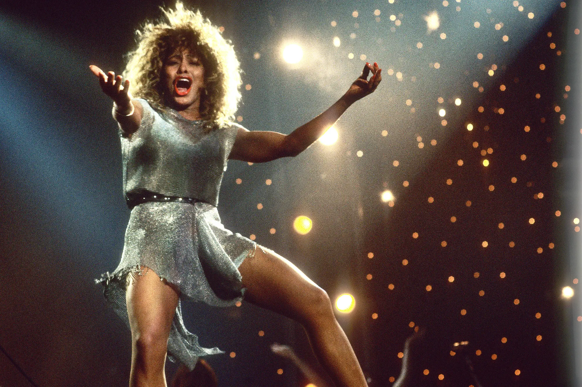 Tina Turner mid song in concert with her hands raised wide