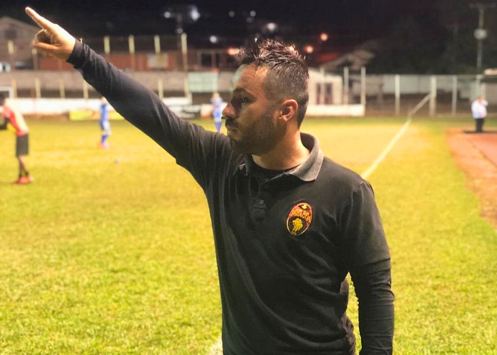 Treinador Gabriel David passando instruções táticas na beira do campo durante jogo oficial de futebol.