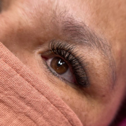 Close-up of eye with long eyelashes, brown iris, and eyebrow, beauty treatment.