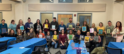 Large group holding art projects behind blue tables.