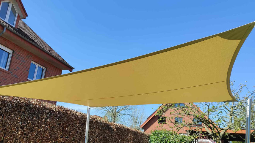 Gelbes Sonnensegel im Garten mit Aluminiummasten mit Höhenverstellung an drei Ecken. Wir sehen das Segel von unten, dahinter Häuser und strahlend blauen Himmel in Osnabrück. 