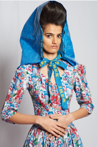 A model posing in in a long-sleeved blue and red floral dress and a headpiece made from an Ikea bag, from the Batsheva Fall 2022 collection presentation