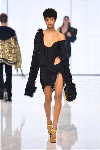 A female model walking down the runway in a black deconstructed mini dress from the  Balmain Spring 2022 collection