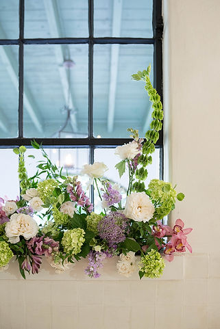 Garden-inspired floral installation with orchids, roses, hydrangeas, and seasonal blooms beneath a window.
