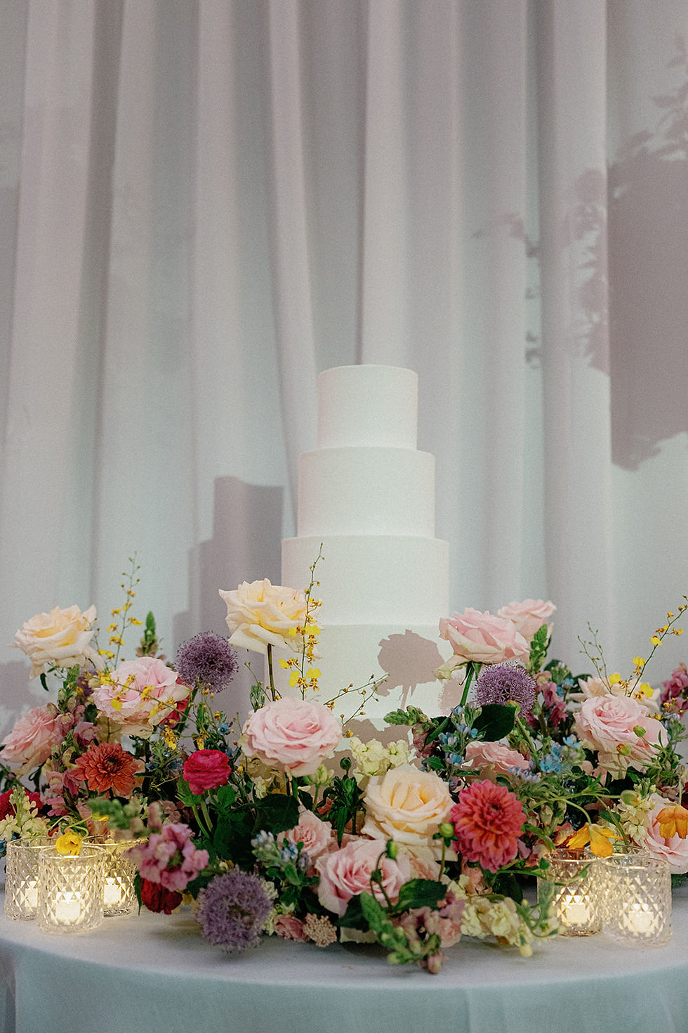 White wedding cake surrounded by colorful spring flowers and candlelight.