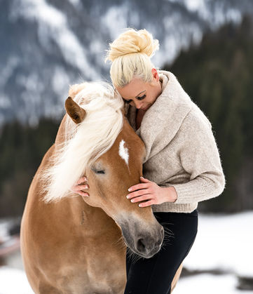 Inniger Momemt währen eine Pferdeshootings Frau umarmt liebevoll ein Haflinger Pferd im Schnee