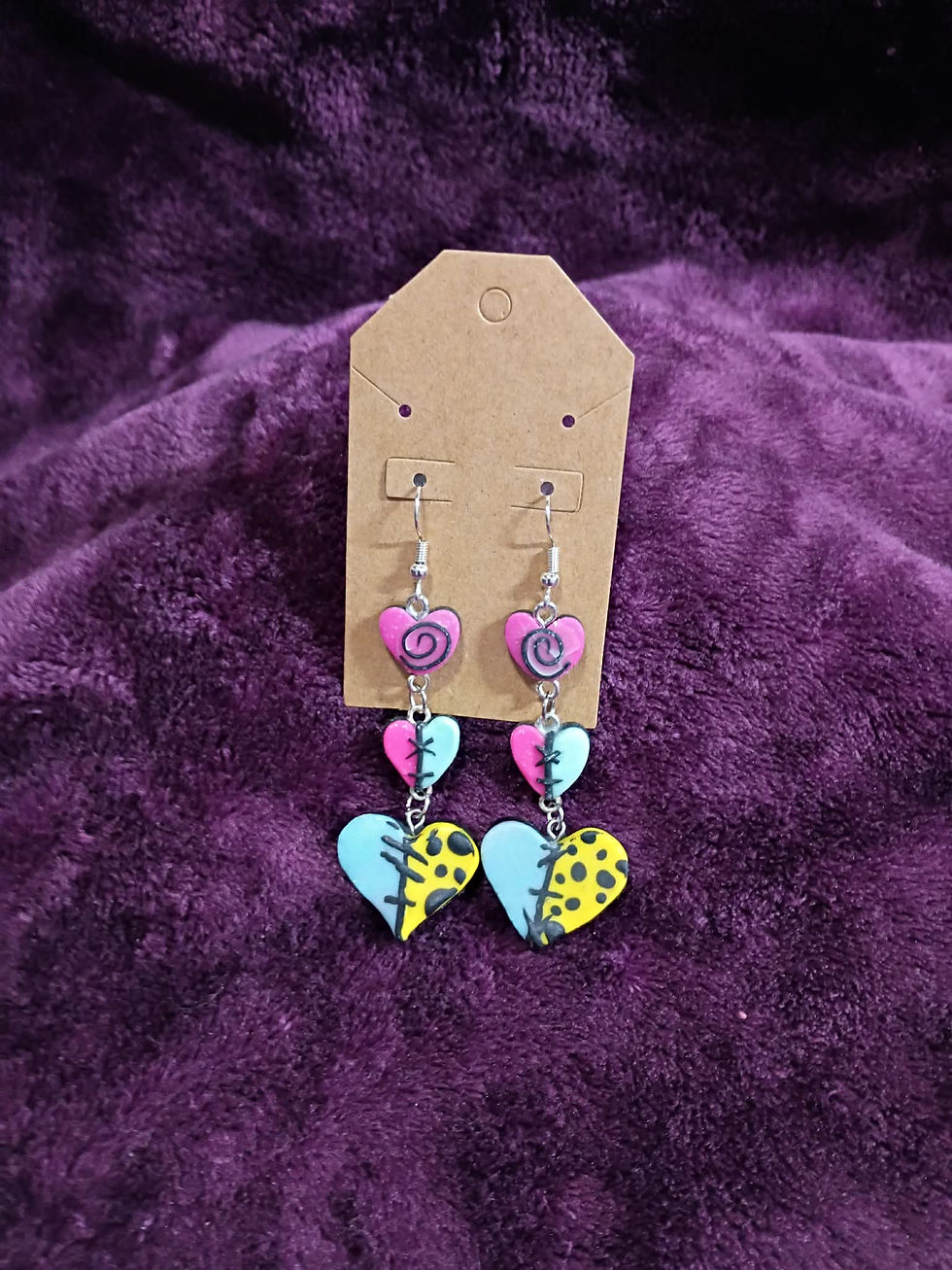 Thumbnail: Triple-heart patchwork dangle earrings with vibrant colors and hand-sculpted stitches against a purple velvet background.