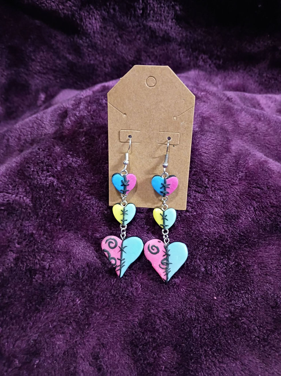 Thumbnail: Triple-heart patchwork dangle earrings with vibrant colors and hand-sculpted stitches against a purple velvet background.