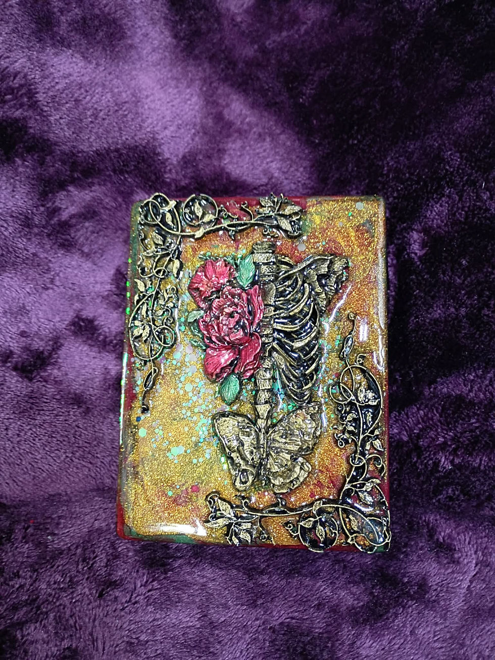 Sculpted resin box lid with a skeleton, roses, and gold vines on a glittery background, set against purple velvet.