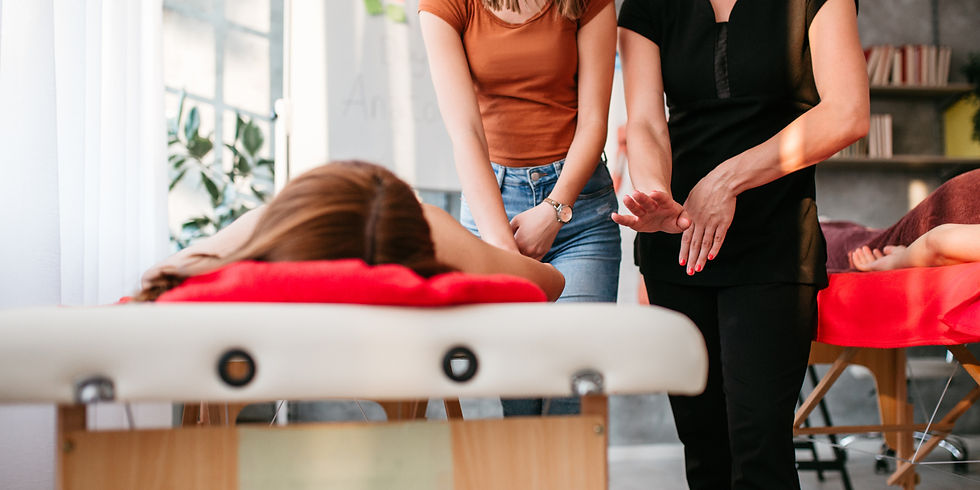 Two women perform a calming healing session over a client lying on a massage table in a bright spa room.