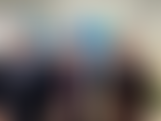 A imagem mostra três homens em um ambiente interno, que parece ser um escritório ou sala de reuniões, posando para uma foto. O primeiro homem (à esquerda, identificado como Paulo Protasio, Presidente da CISBRA) veste um terno azul-marinho com uma camisa azul-clara. O segundo homem (ao centro, identificado como o Embaixador João Luiz de Barros Pereira Pinto) veste um terno azul-escuro com uma camisa branca e uma gravata vermelha estampada. O terceiro homem (à direita, identificado como Ricardo Mota, Vice-Presidente da CISBRA) veste um paletó marrom e uma camisa cinza-clara. Atrás deles, na parede, há três grandes mapas mundi em tons de azul, verde e amarelo, que parecem ser mapas temáticos ou de dados geográficos. Entre os mapas há textos descritivos ou legendas. No canto inferior direito da imagem, há uma planta em vaso, e no canto inferior esquerdo, garrafas de água sobre uma mesa. Em resumo, a foto registra os três indivíduos lado a lado em um encontro formal, com mapas globais