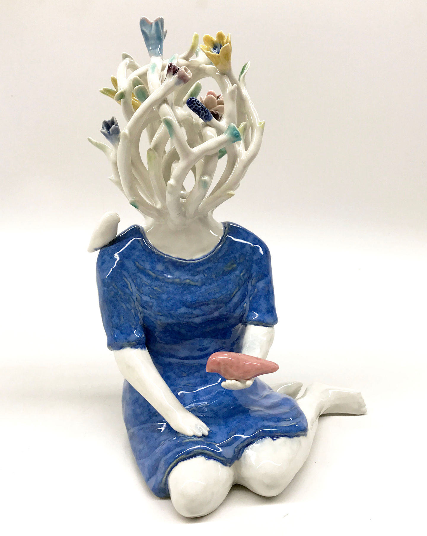 Porcelain seated female figure in blue with white lattice head and flowers and leaves. Holding a red bird in hand.