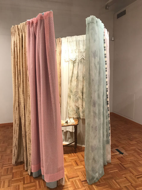 Sculptural form made from wood armature and found curtain walls with an opening the invites viewers inside where a small table holding cast beeswax objects, porcelain child's shoes and lace sits in the center