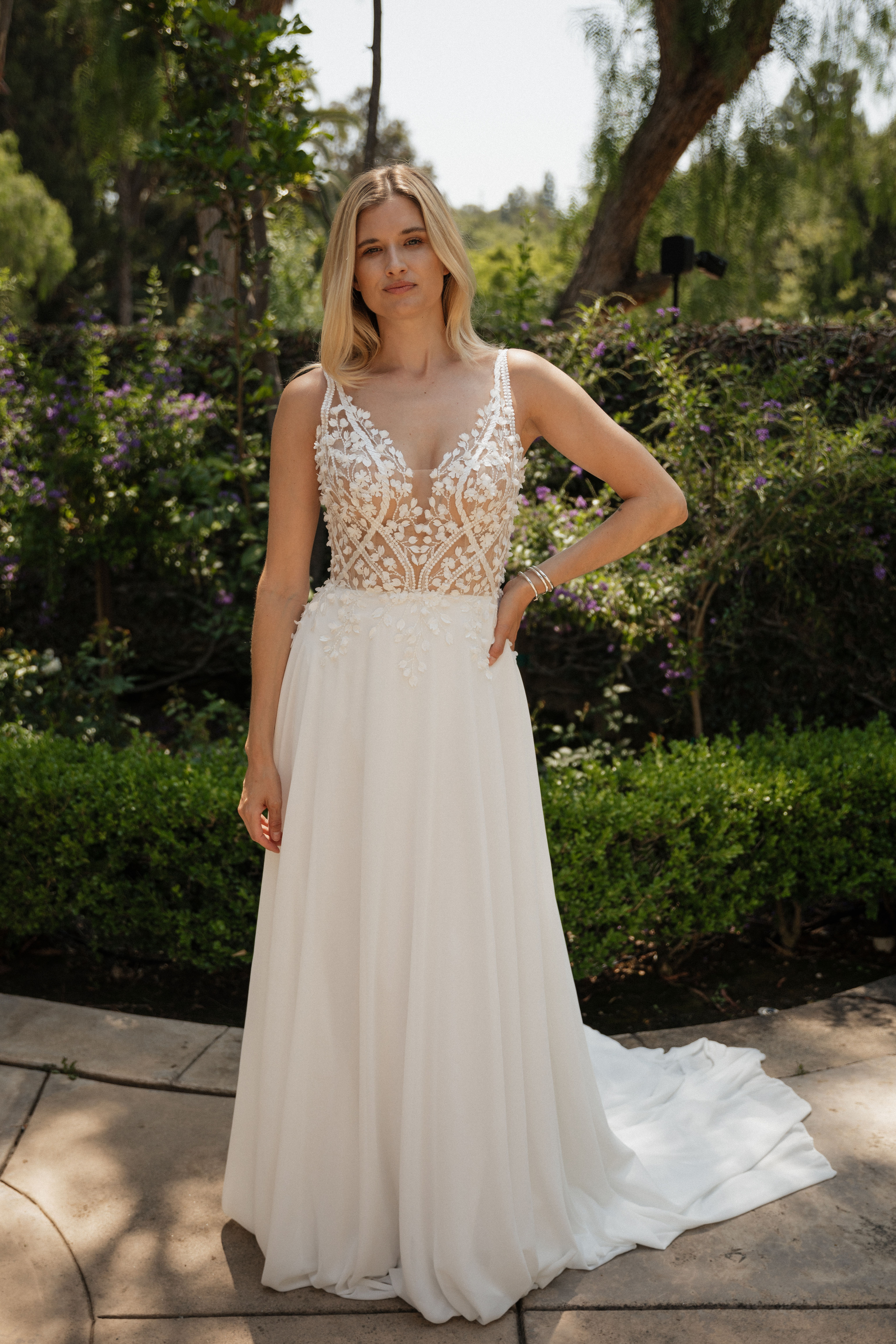 Tati | S25510
Gown Info
Crafted with exquisite detail, this gown features chiffon layered over a soft lining, with a bodysuit inside ensuring both comfort and elegance. Adorned with intricate 3D embroidered lace, the gown exudes timeless sophistication and intricate craftsmanship. The deep V-neckline adds a touch of allure and modernity, beautifully framing the neckline. Flowing into a small A-line skirt, this silhouette offers a blend of grace and understated charm, perfect for the bride seeking a classic yet contemporary bridal look.

Material
Chiffon

Color & Size
Shown in Ivory/Nude

Also available in Ivory/Ivory

Available Sizes: 2 - 28 / 14W - 32W Size Chart