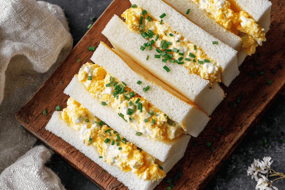 Tamago sando sandwich on a wooden board, yellow egg filling with green chives, landscape aspect ratio, warm neutral tones.