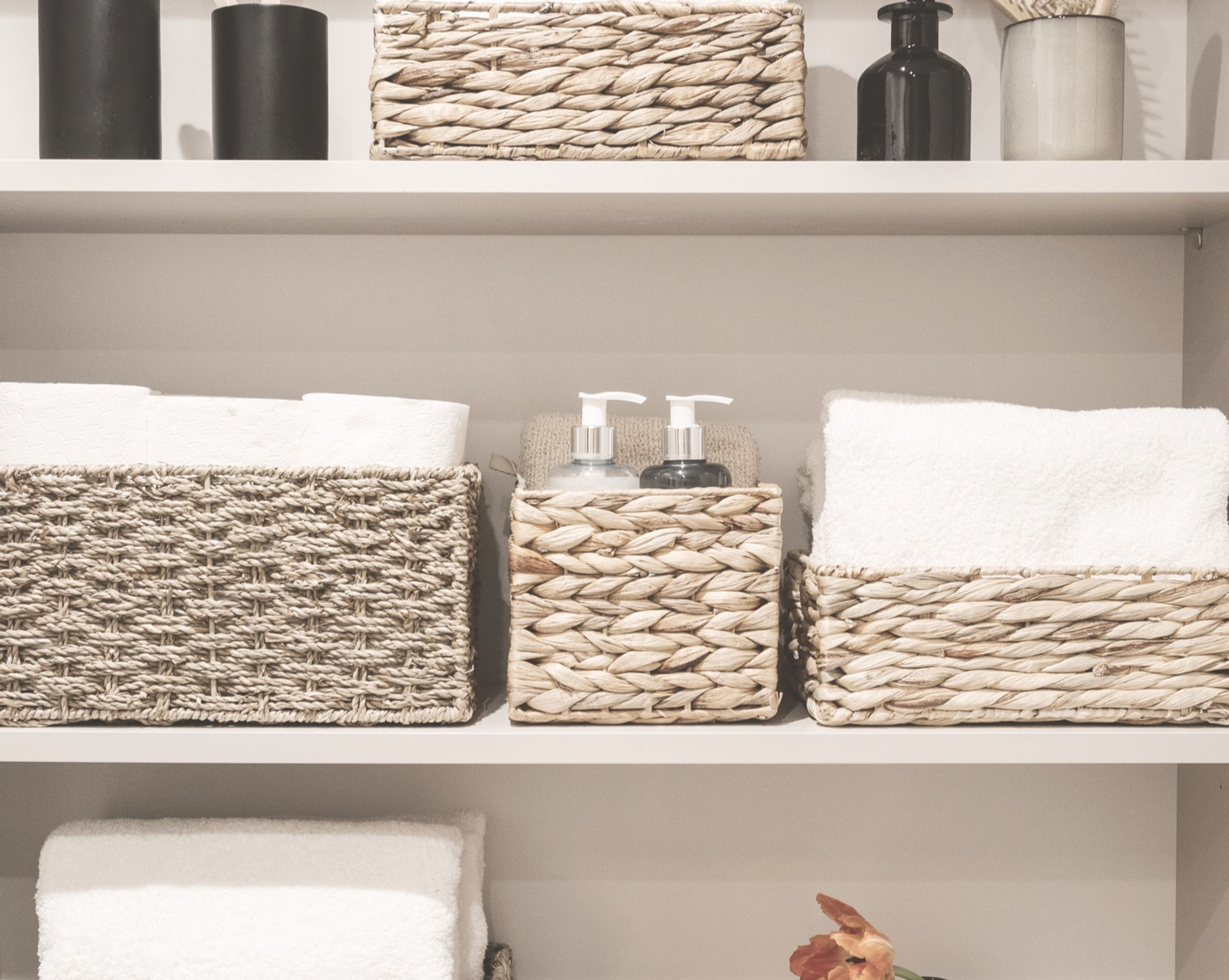 Household items, toilet paper rolls, white bath towels and cosmetics bottles on shelves in