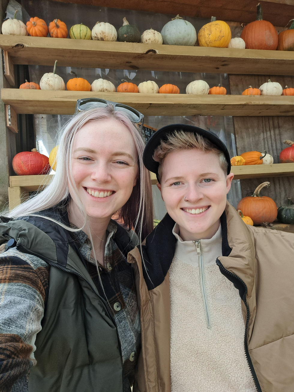 2 girls smiling in a selfie in front of pumpkins on a shelf