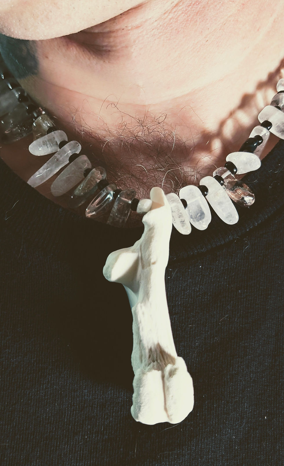 Thumbnail: A unisex necklace featuring a large white wild boar ankle bone pendant, clear and smoky quartz chips, and black beads on a ma