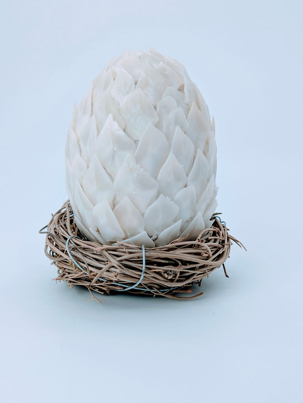 A small handcrafted Dragon Egg sculpture made of overlapping white Longnose Gar scales sitting in a bird's nest.