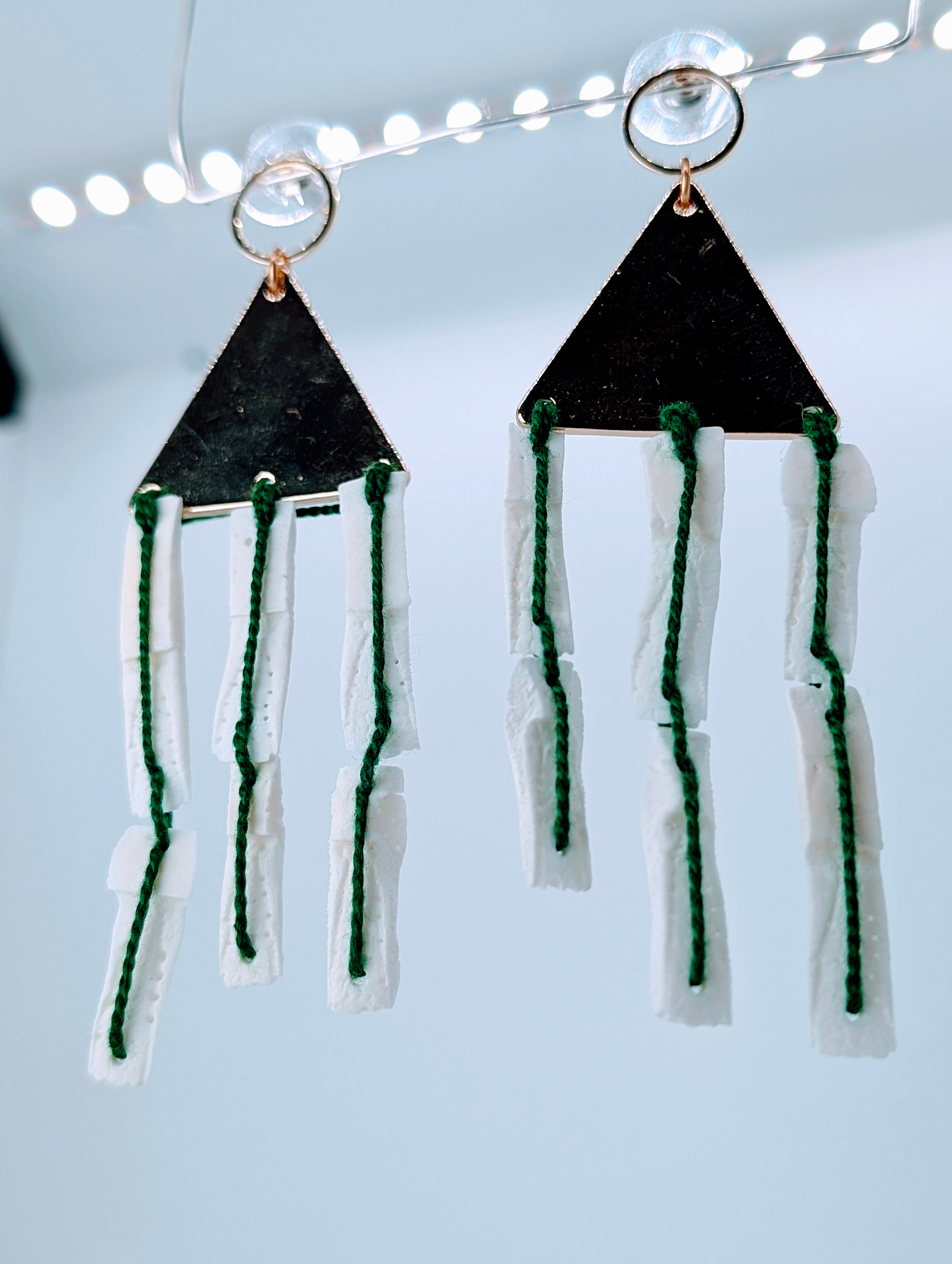 A pair of 3.5-inch drop earrings featuring white armadillo scutes attached to gold-tone triangles with emerald green thread a