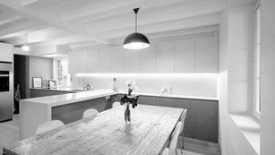 Sala da pranzo moderna con tavolo in legno, sedie minimaliste e camino rustico integrato sotto soffitto con travi a vista in.