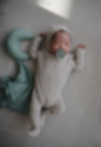 Baby in een beige pakje met een speen, een muts en een groene halfmaanvormige kussen