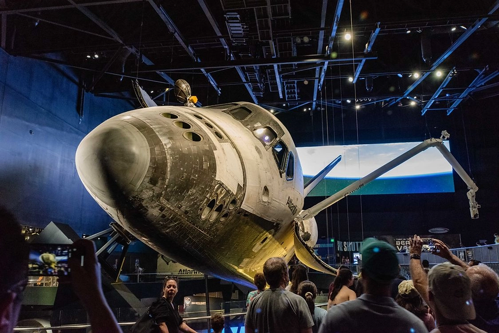 Space shuttle Atlantis on display in a dark museum, with visitors photographing it under bright lights.