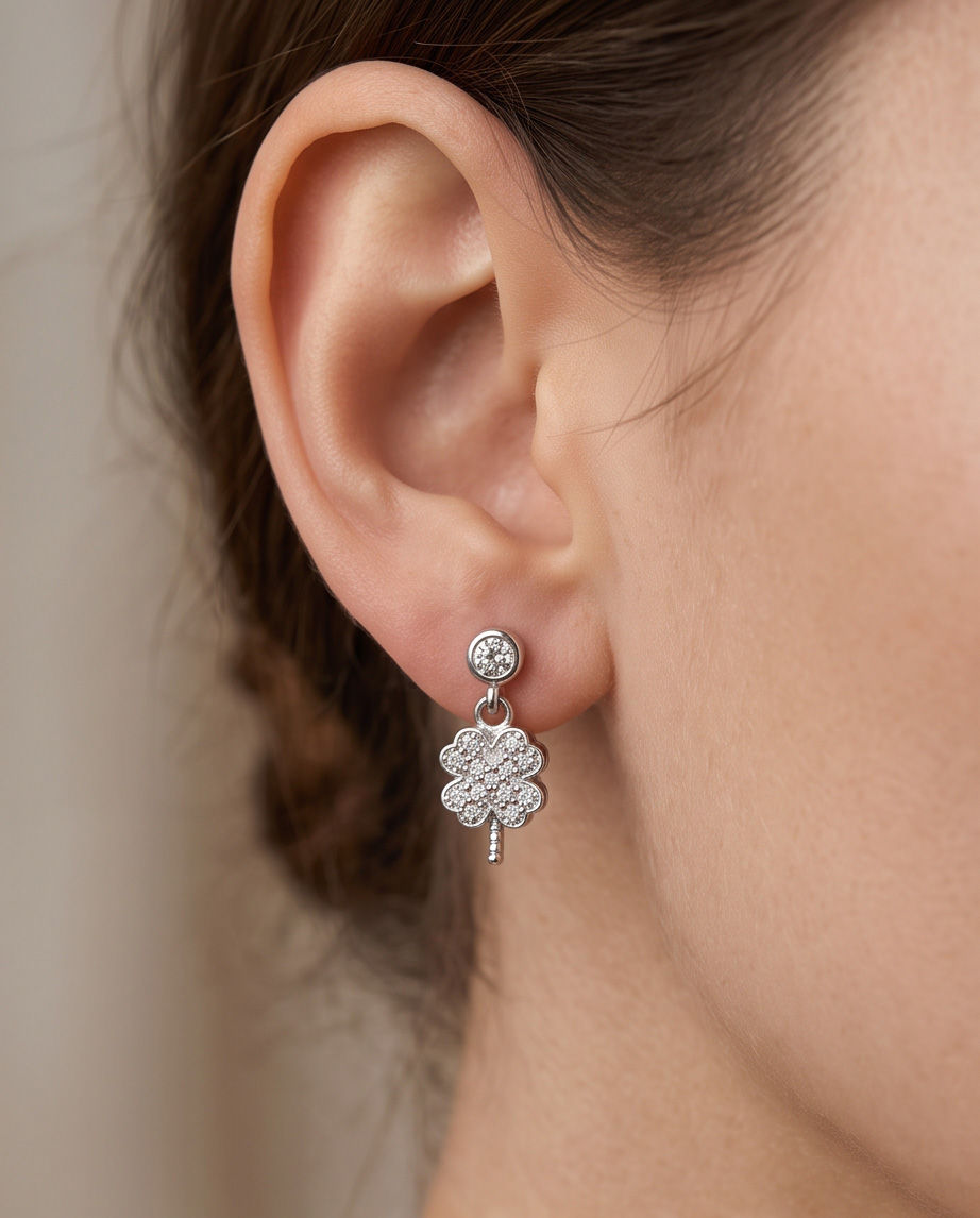 Parlak zirkon taşlarla bezenmiş, sallantılı dört yapraklı yonca figürlü 925 ayar gümüş çivili küpe ve klips detayı.