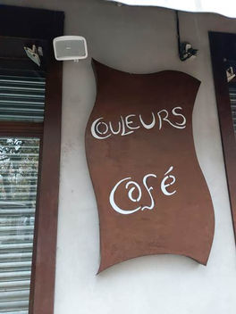 Panneau marron : COULEURS Café en écriture blanche, devant un café, STORM SONO.