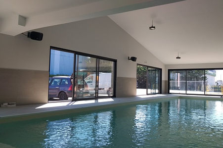 Piscine intérieure avec de grandes fenêtres et une voiture garée à l'extérieur.