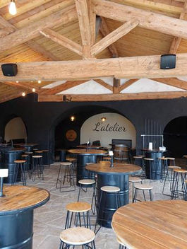 Un restaurant L'Atelier avec tables rondes et tabourets en bois; NOS REALISATIONS