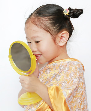 Smiling asian child girl in traditional thai dress using mirror isolated on white backgrou