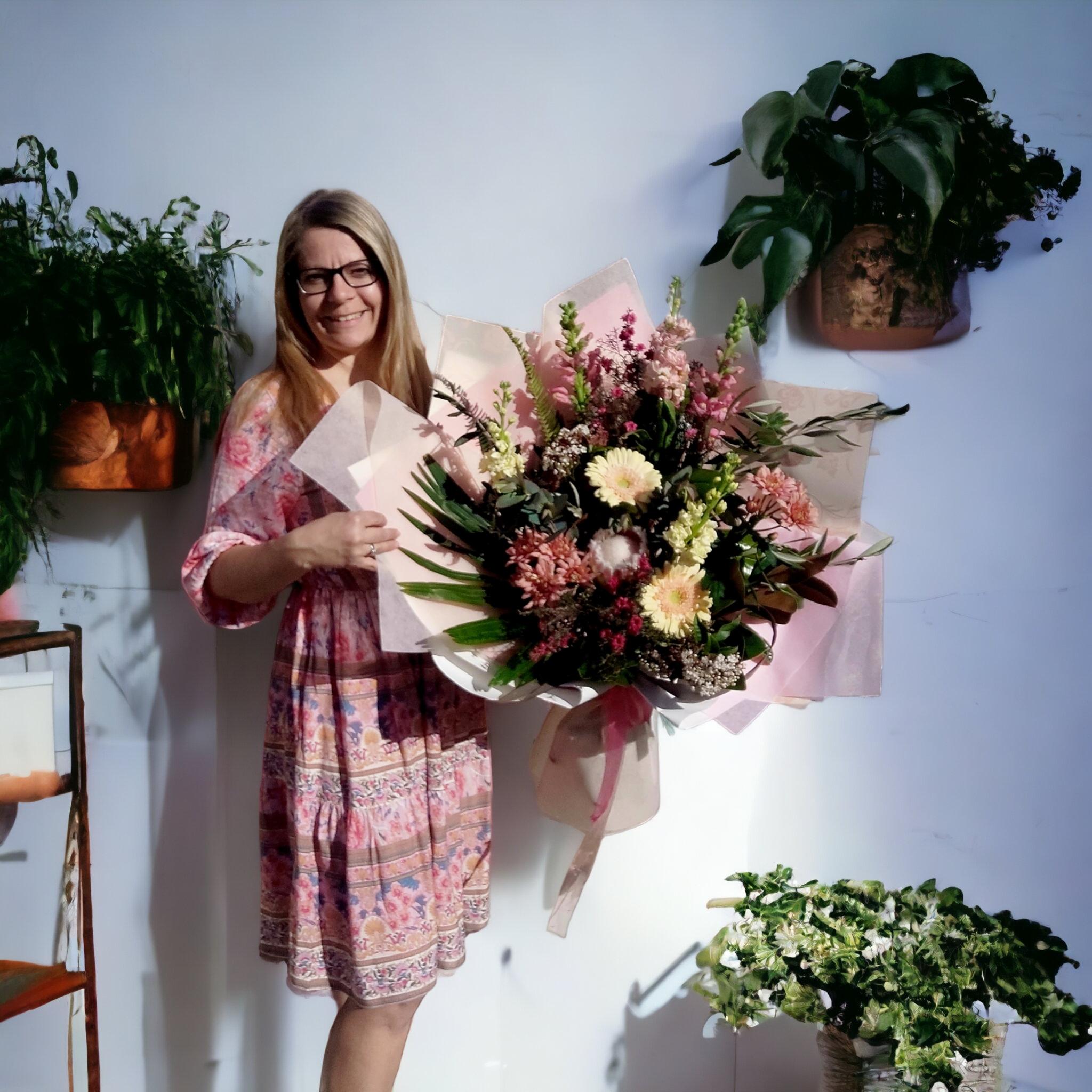 Kat holds a floral bouquet made with pink and cream flowers with green foliage, wrapped in matching paper and ribbons.