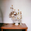 Thumbnail: A dried floral arrangement of white, beige and cream flowers and foliage, presented in a vase.