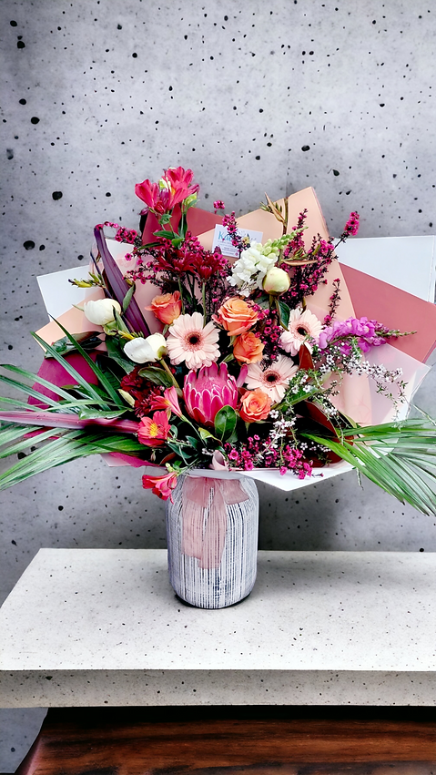 A fresh bouquet of pink, peach and magenta flowers with foliage, wrapped in matching paper.