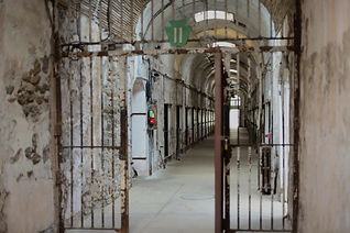 "Dark, decaying prison with barred windows and concrete walls set against a mountainous backdrop, echoing real isolation-themed haunts in the Mountain region"