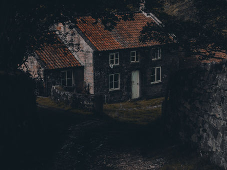 "A dark, moody photograph of an old Victorian-style brick jail under a full moon, with arched windows, a central tower, and leafless trees surrounding the haunted structure."