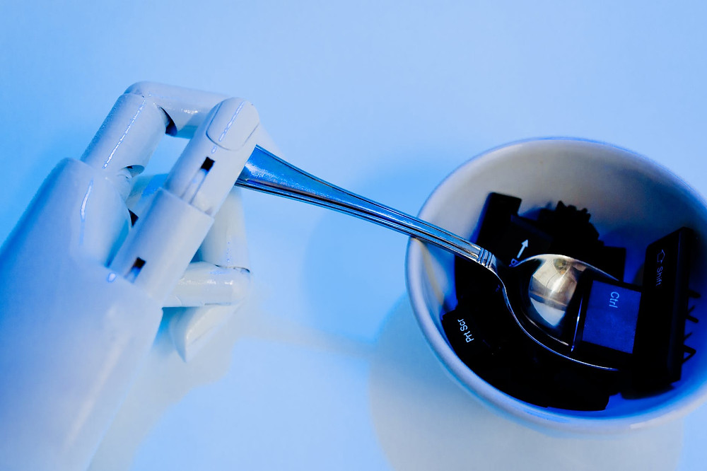White robotic hand on the left, holding a spoon, holding computer buttons on a bowl